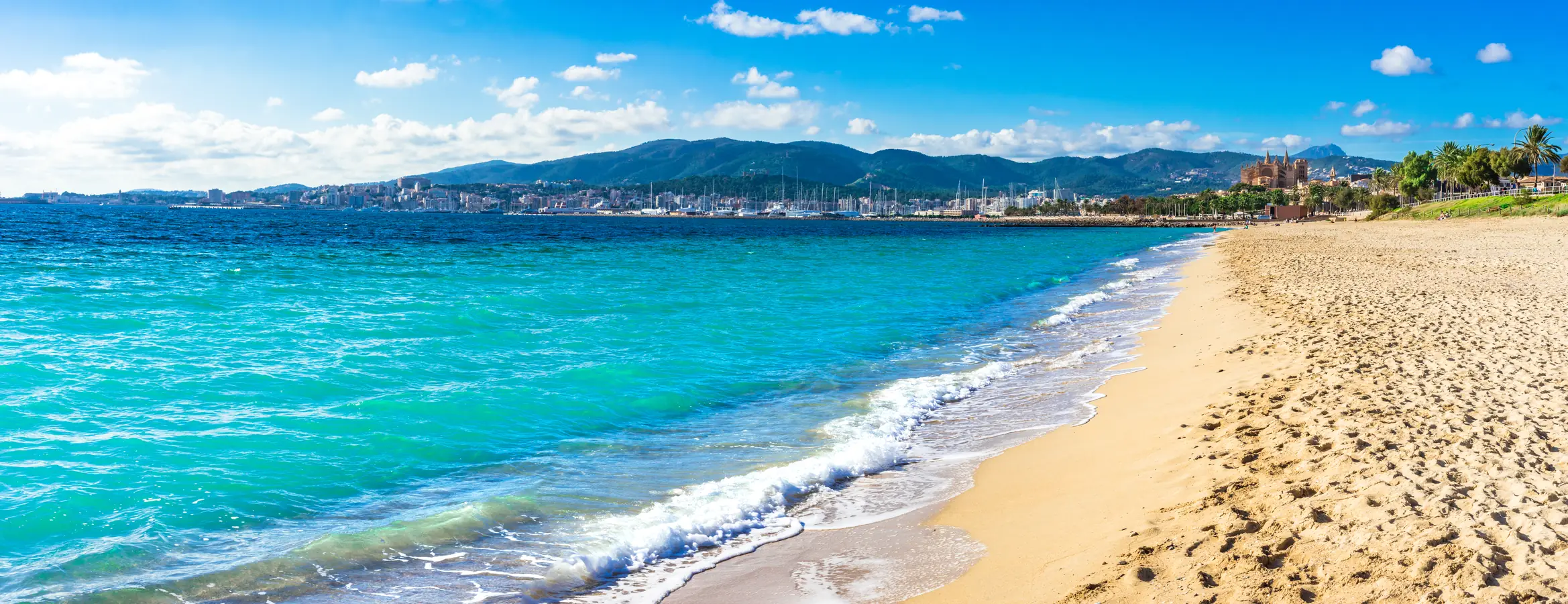 Sandstrand und türkisfarbenes Meer vor Palma, dahinter Hafen, Kathedrale und die Berge